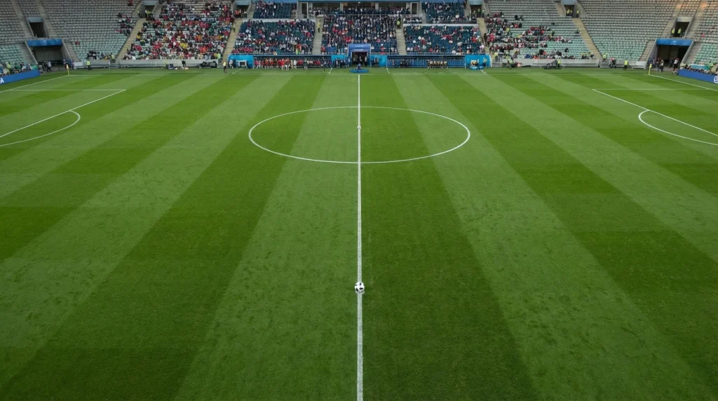 Close-up van een voetbalveld met krijtlijnen en een bal op de middenstip bij daglicht